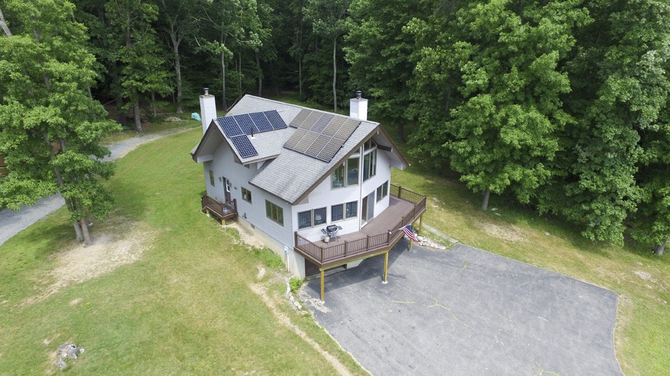 aerial view of secluded cabin with solar panels and a custom deck surrounded by woods