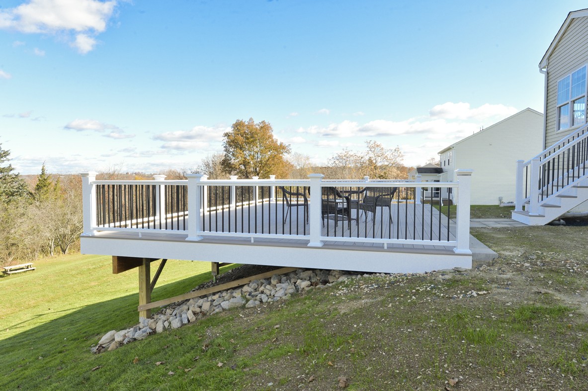deck overhanging on a backyard hill with white railings and gray decking